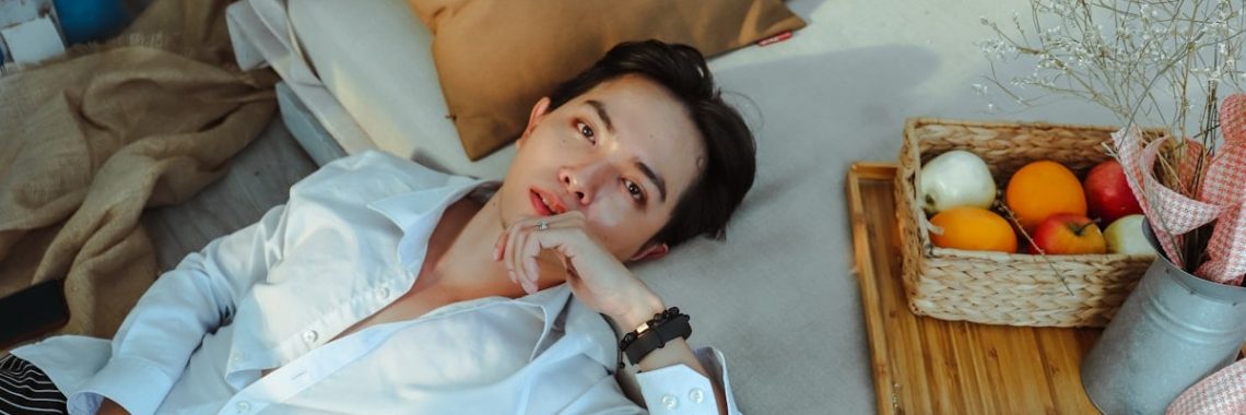 a man laying on a bed next to a basket of fruit